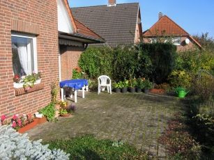 Ein Backsteinhaus mit einer Terrasse mit Tisch und Stühlen davor.