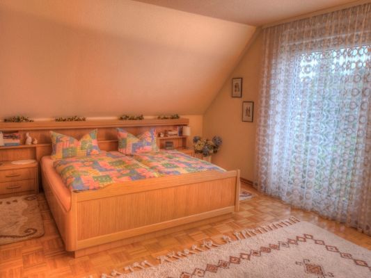 Ein Schlafzimmer mit einem Bett, Nachttischen, Vorhängen und einem Fenster.