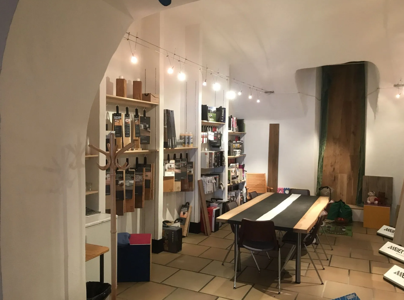 Ein Zimmer mit Steinboden, Lichterketten, Regalen voller Flaschen und einem grossen Esstisch mit Stühlen.