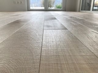 Eine Ansicht aus der Froschperspektive auf helle, holzmaserige Dielen in einem hell erleuchteten Raum mit einem Fenster im Hintergrund.
