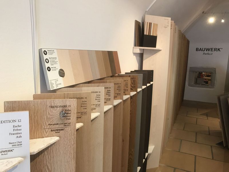 In einem Ausstellungsraum sind Muster von Holzfussböden in verschiedenen Beiztönen in einer Reihe auf Regalen angeordnet.