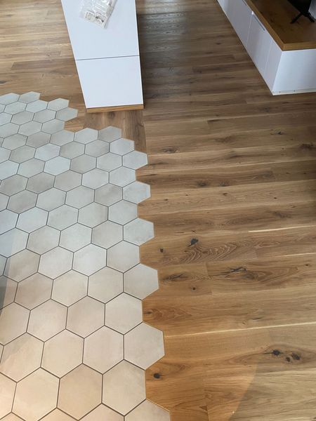 Ein fliessender Übergang zwischen hellgrauen sechseckigen Bodenfliesen und warmtonigen Holzplanken in einem modernen Interieur.