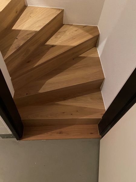 Eine hölzerne Treppe, die sich zwischen weissen Wänden nach oben windet, von unten nach oben betrachtet.