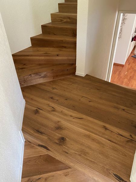 Eine Holztreppe mit breitem unteren Podest, die durch natürliche Holzmaserung und weiße Wandakzente besticht.
