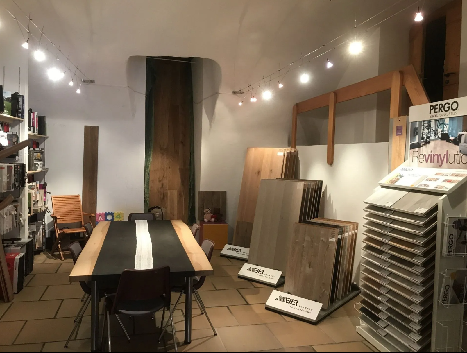 Ein Ausstellungsraum mit Konferenztisch, verschiedenen Holzfussbodenmustern und Lichterketten an einer weissen Decke.