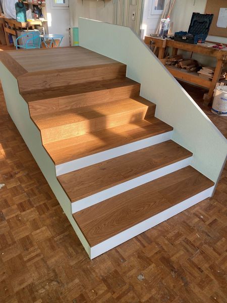 Eine Holztreppe mit weissen Setzstufen und Seitenwänden in einer Holzwerkstatt.