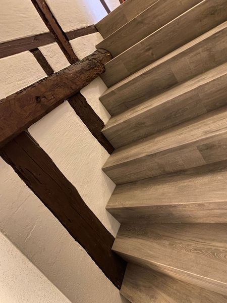 Links davon befindet sich eine Treppe mit Stufen in Holzoptik und eine rustikale, dunkle Holzbalkenkonstruktion.
