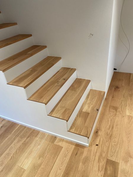 Eine Holztreppe mit weissen Setzstufen neben passendem hellen Holzboden.