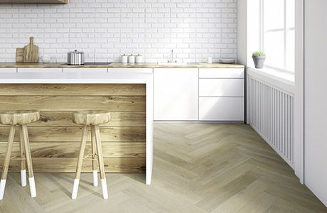 Eine helle Küche mit einer Kücheninsel aus Holz, zwei Barhockern, weissen Schränken, Ziegelwänden und Fischgrätparkett.