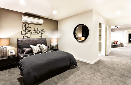 Ein modernes Schlafzimmer mit dunklem Bett, grauem Teppichboden, einem runden Spiegel an der Wand und einer Klimaanlage über dem Bett.