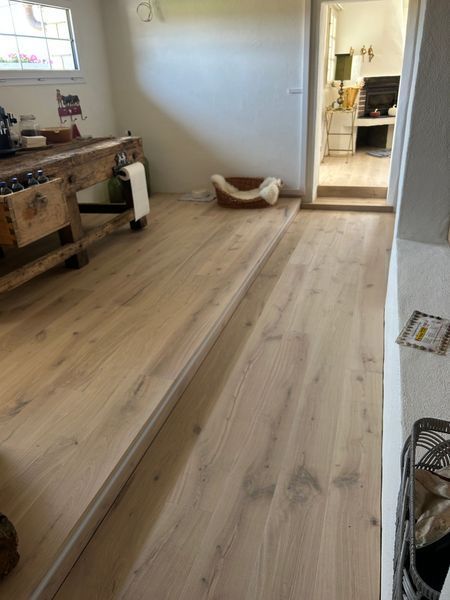 Ein Zimmer mit hellem Holzboden, einer Stufe zu einem Arbeitsbereich, einer rustikalen Holztheke und einem Haustierbett in der Ecke.