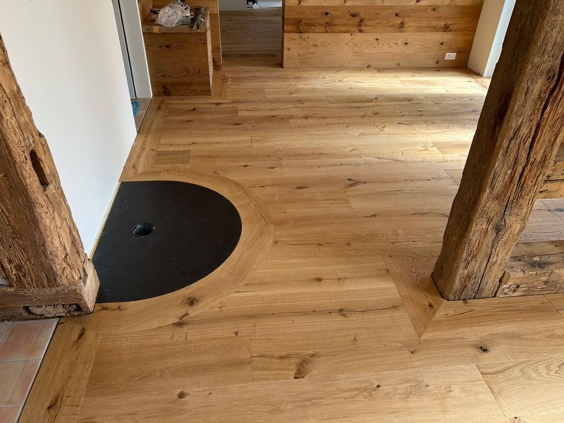 Holzfußboden mit einem gebogenen, schwarzen, halbkreisförmigen Einsatz, der von Dielen eingefasst ist und sich zwischen rustikalen Holzpfosten befindet.