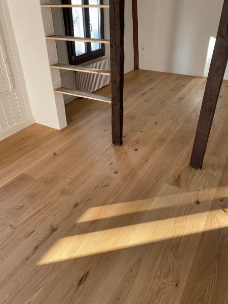 Hellfarbener Hartholzboden in einem Raum mit einer Holzleiter und dunklen Holzpfosten.