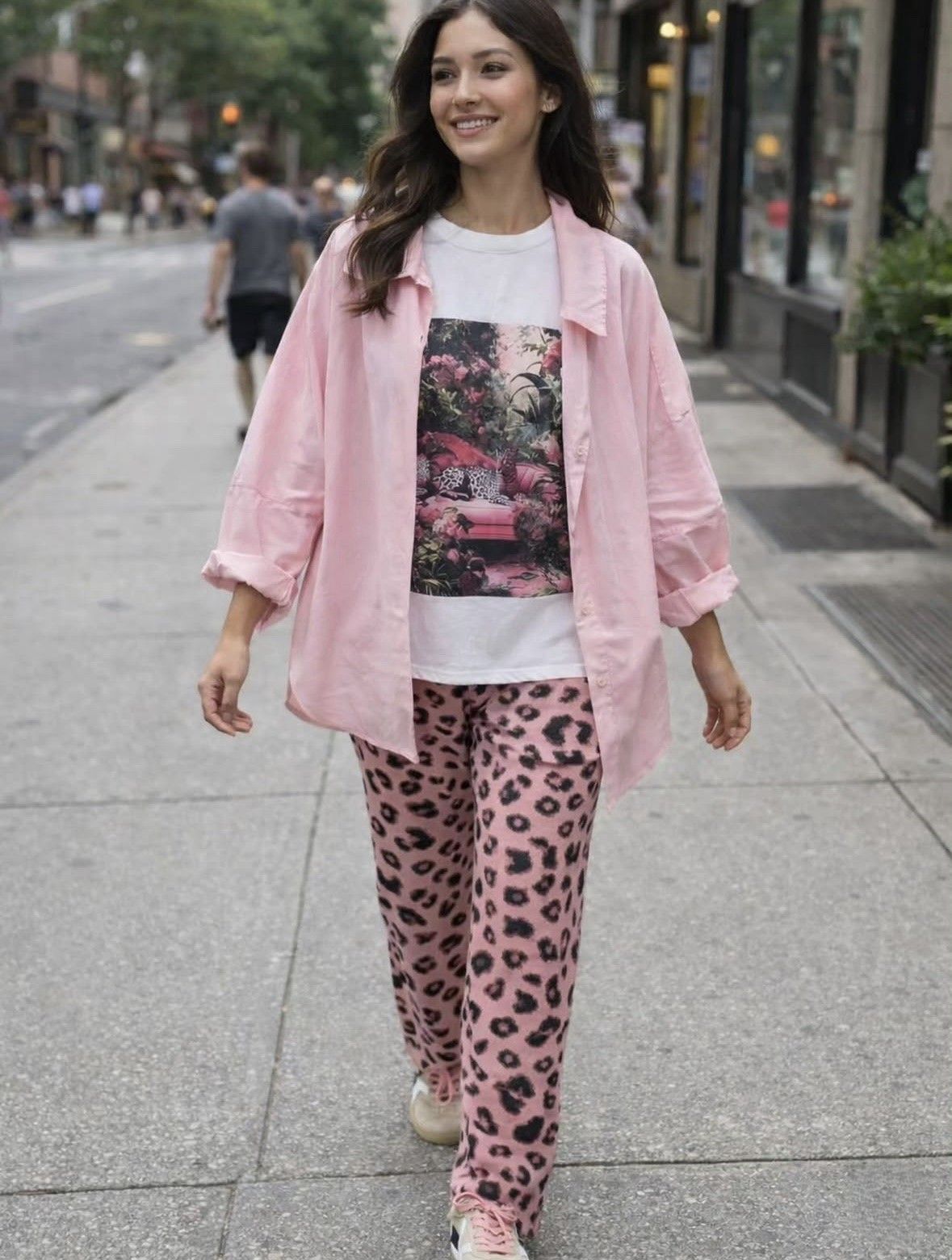 Mujer caminando por una acera de la ciudad con una camisa rosa y pantalones con estampado de leopardo, sonriendo.