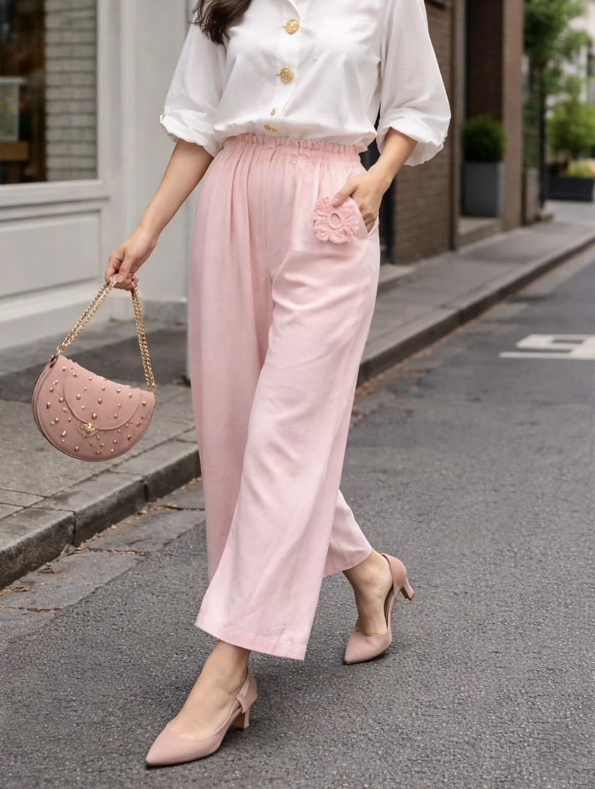 Mujer caminando por la calle con blusa blanca y pantalones anchos rosas, llevando un bolso rosa.