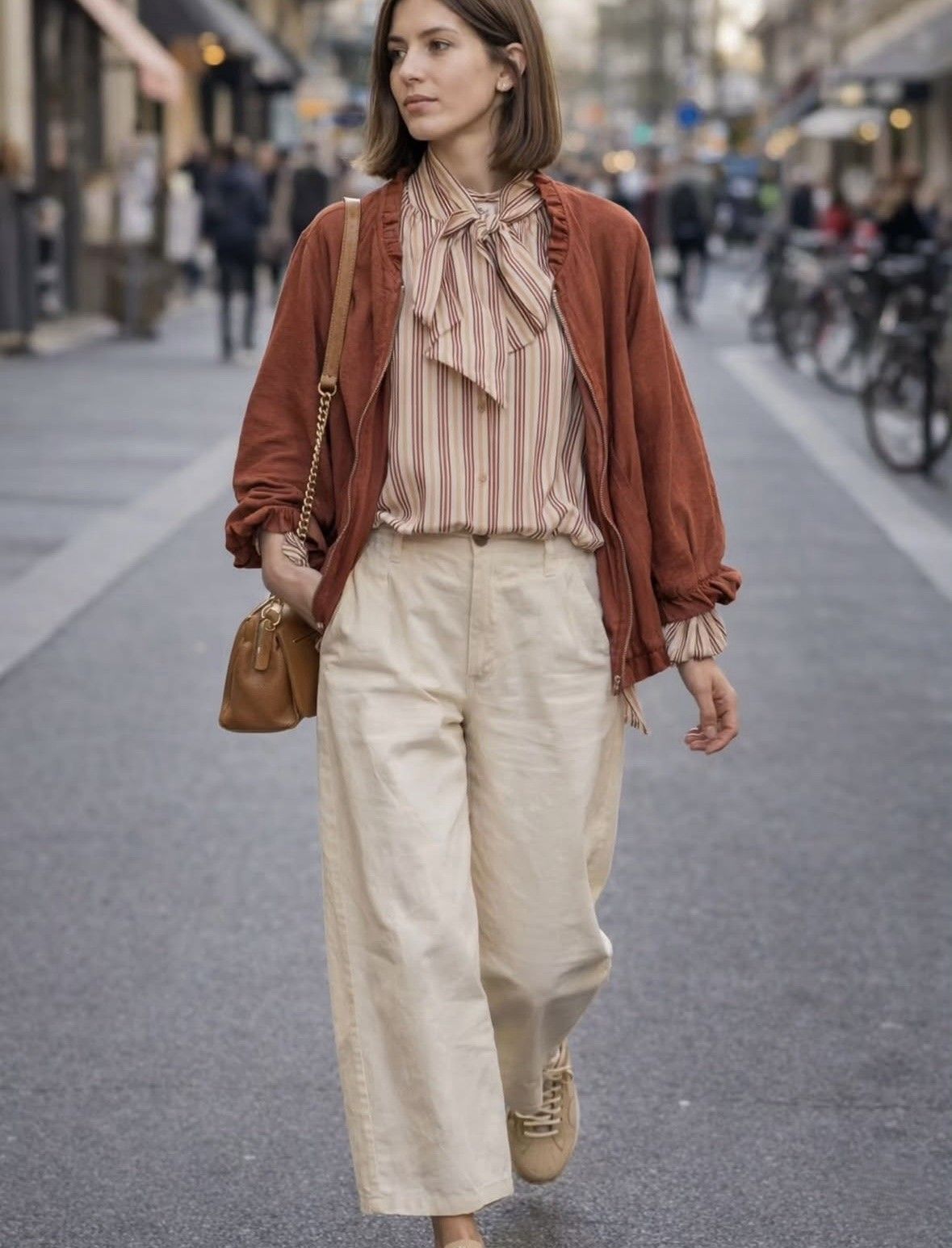 Persona caminando por una calle de la ciudad con un cárdigan color óxido, blusa con volantes, pantalones color crema