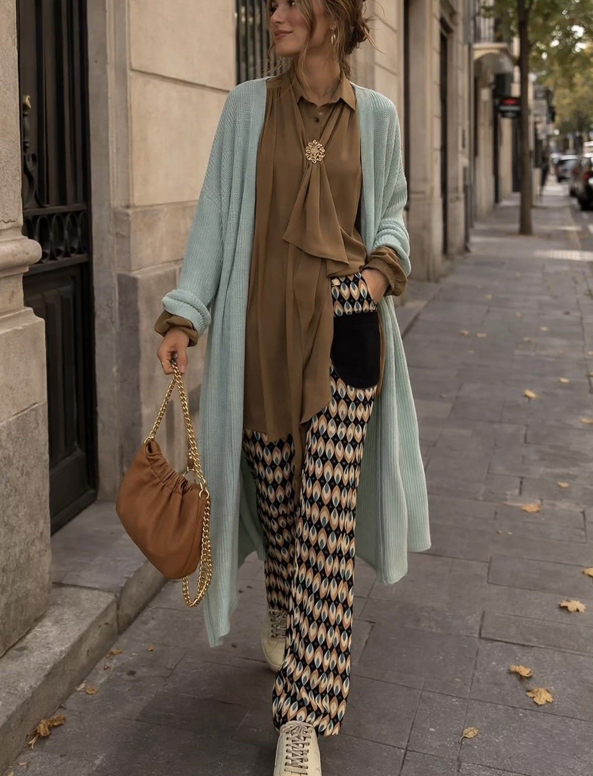Mujer con abrigo color menta y blusa marrón caminando por una acera de la ciudad, llevando un bolso color canela.