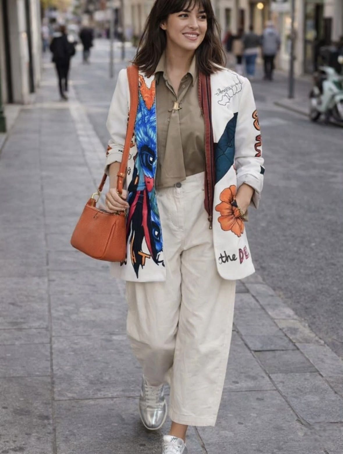 Mujer caminando por una calle de la ciudad, vestida con un traje color crema y una bufanda colorida