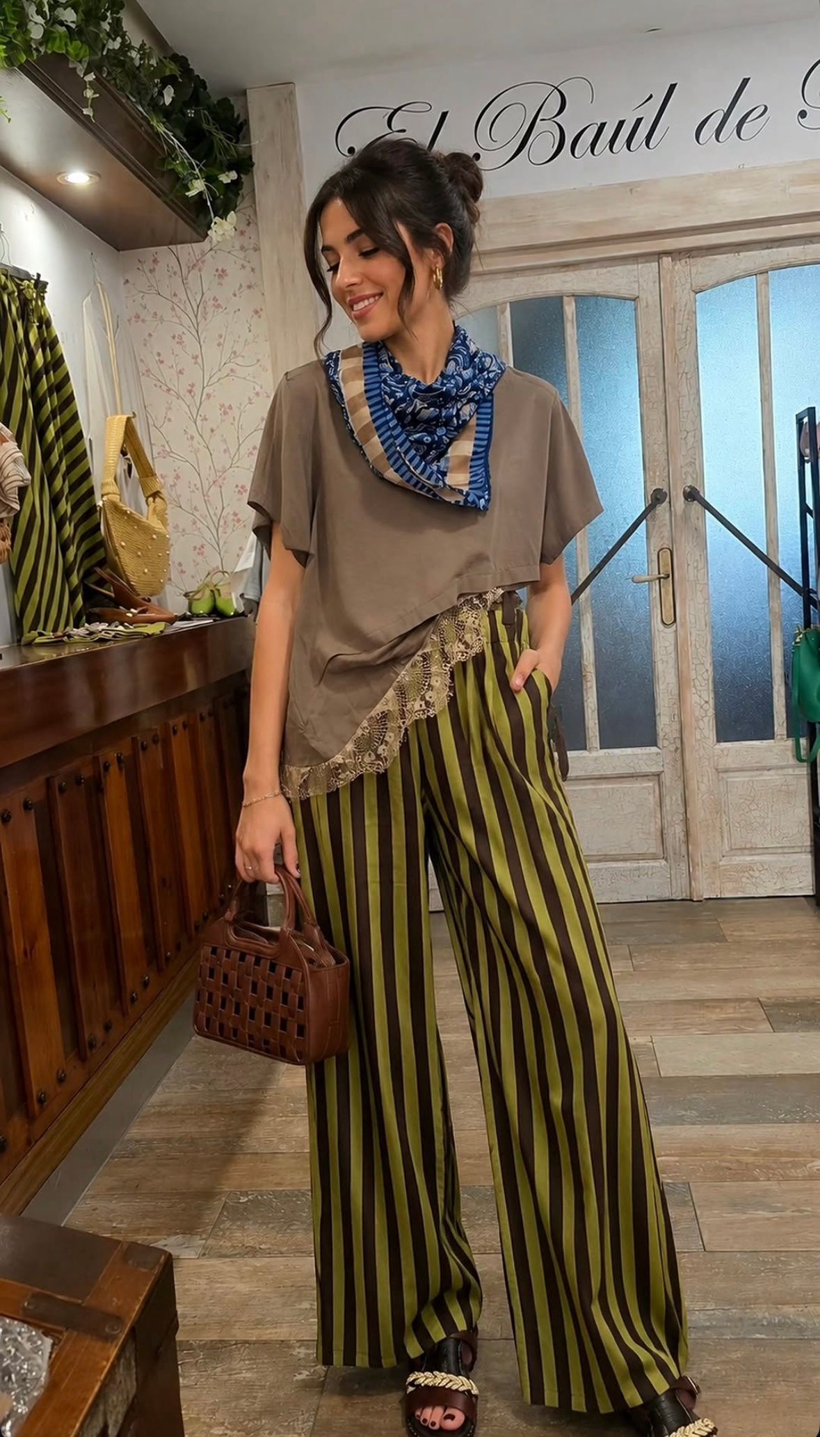 Mujer con un conjunto de rayas posando en interiores con un bolso de mimbre y una bufanda azul.