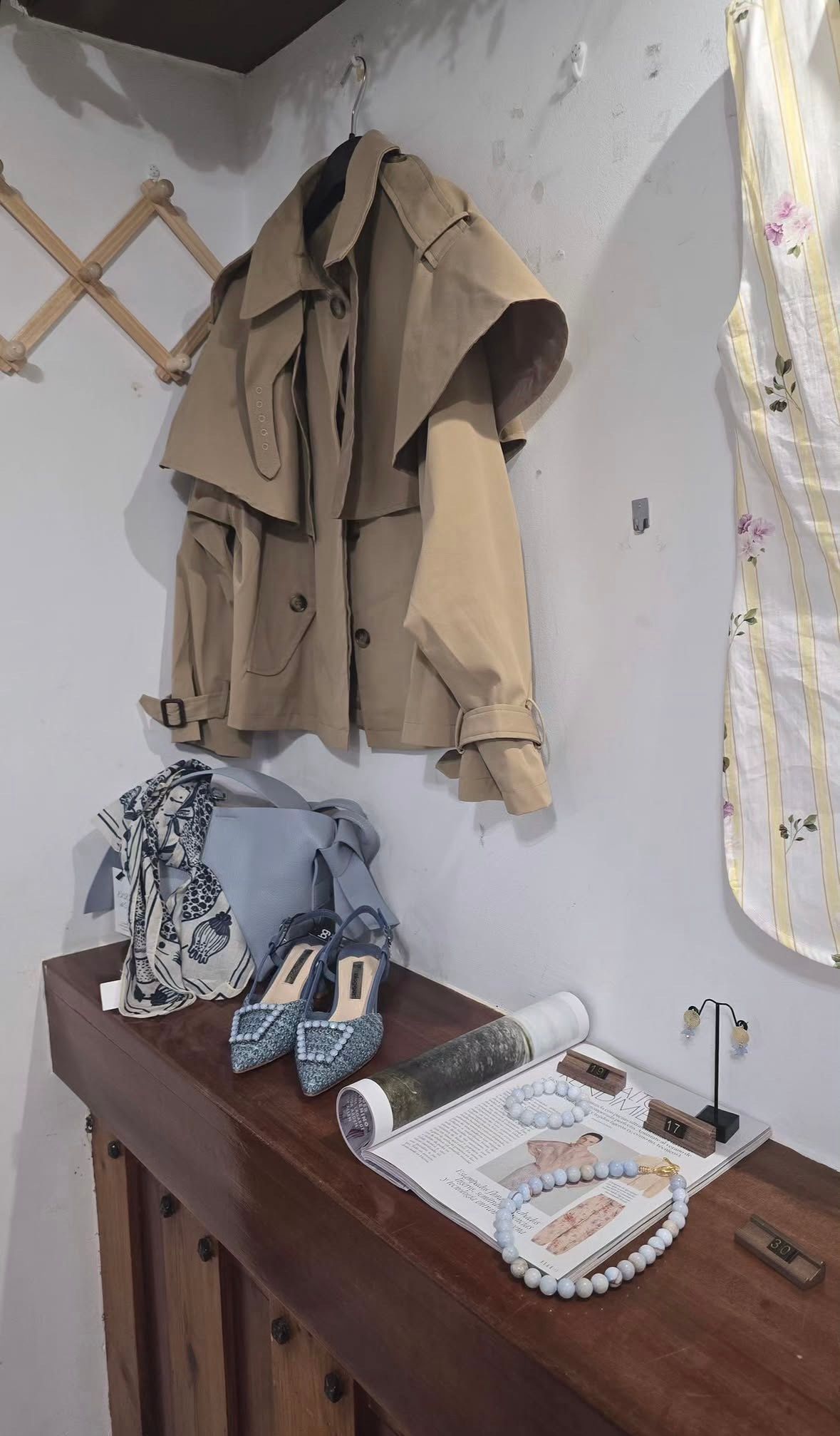 Un abrigo marrón colgado sobre una mesa de madera con ropa doblada y objetos variados encima.
