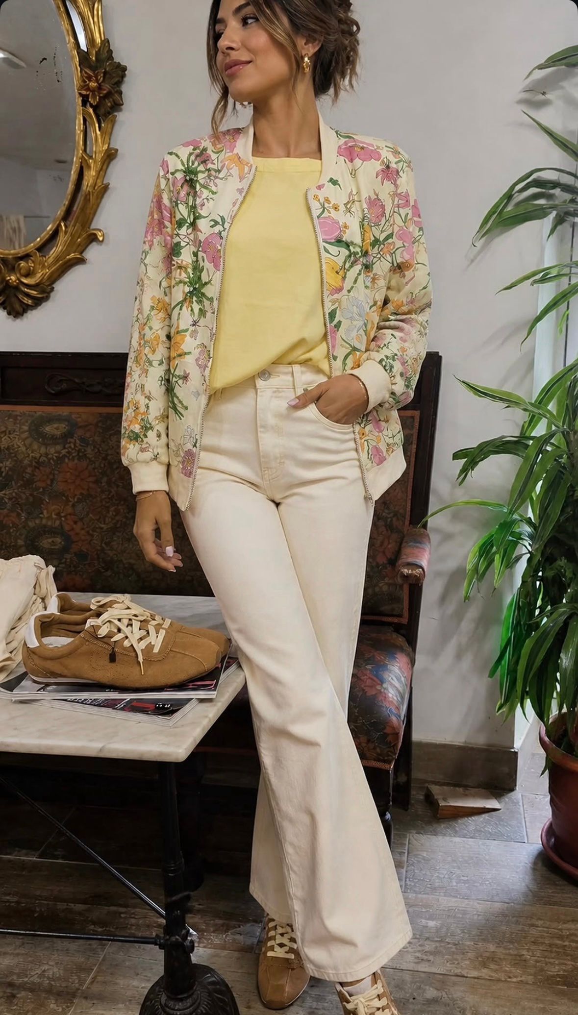 Mujer modelando una chaqueta floral sobre una blusa amarilla con pantalones blancos en una habitación con decoración vintage.