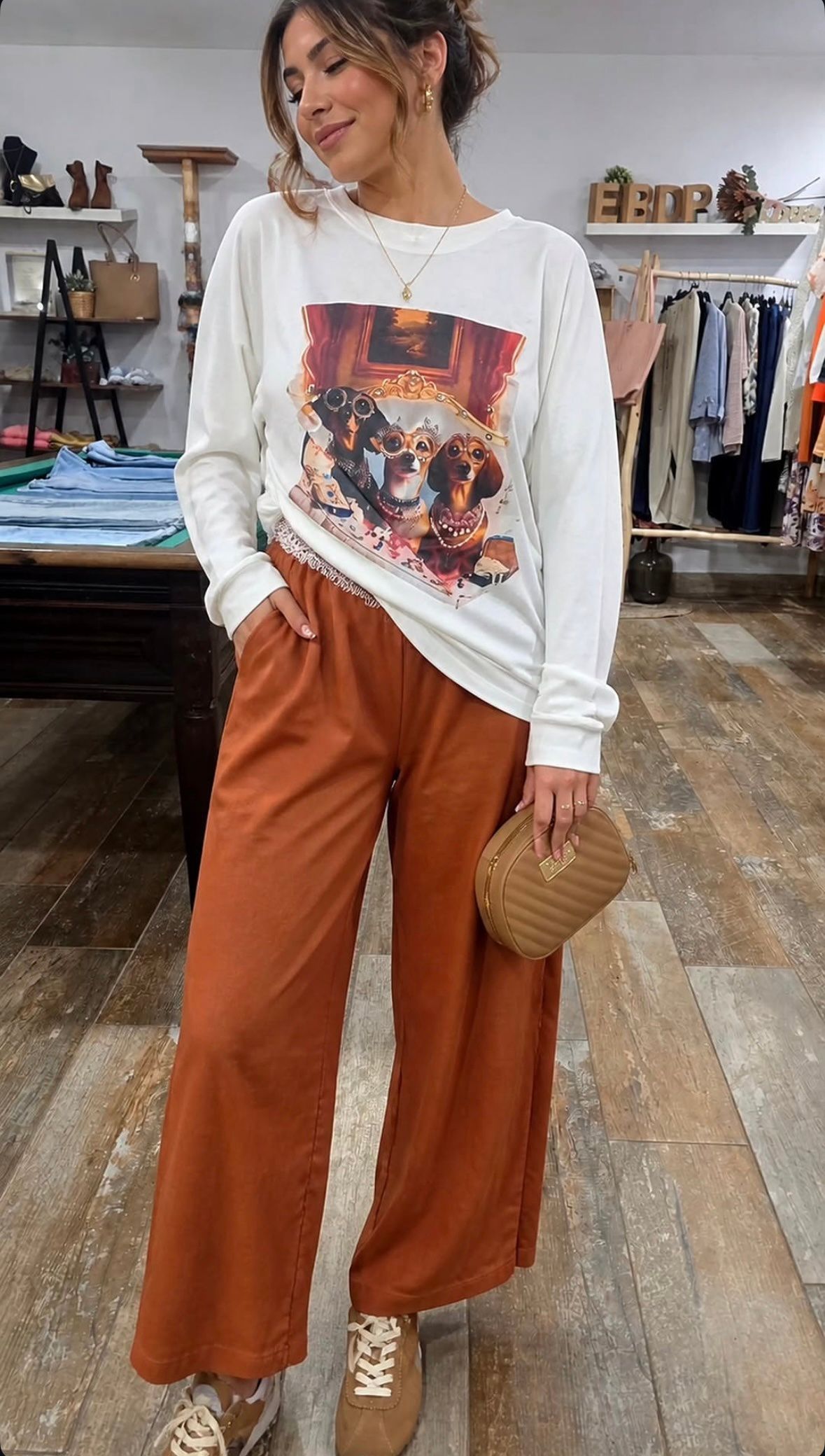 Mujer modelando una sudadera blanca estampada y pantalones anchos color óxido en una boutique de ropa.