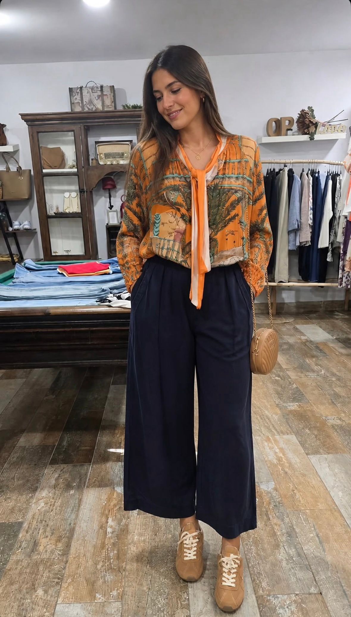 Mujer luciendo una blusa estampada de color naranja, pantalones anchos azul marino y botas color canela