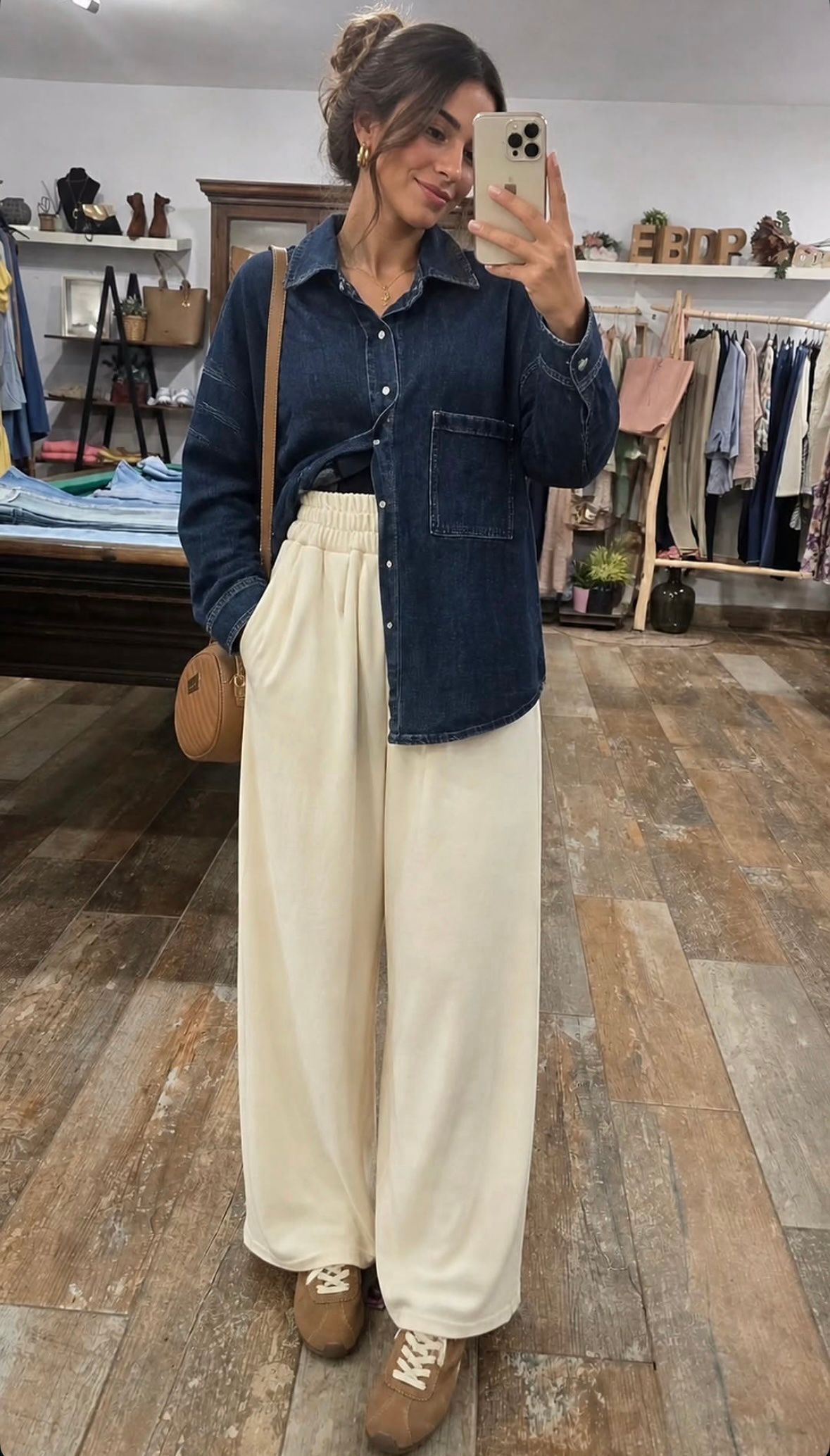 Persona tomándose una selfie frente al espejo con una camisa vaquera, pantalones color crema y botas color canela