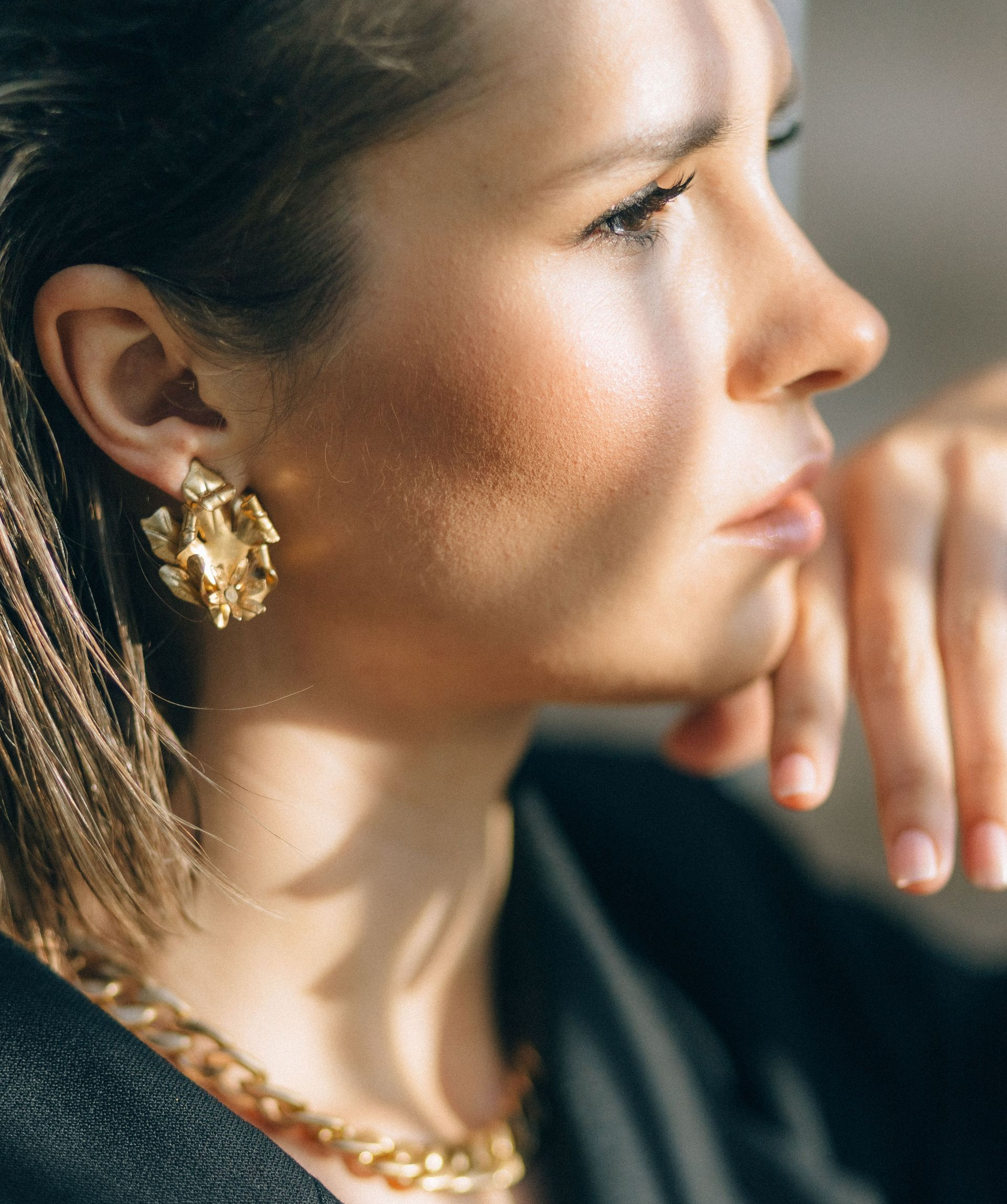 Perfil de una mujer que lleva joyas de oro, apoyando la barbilla en la mano y mirando pensativamente.