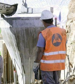 Un trabajador de la construcción que lleva un chaleco naranja y un casco está parado frente a una pared.