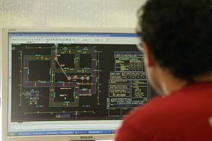 Un hombre con una camisa roja está mirando una pantalla de computadora.