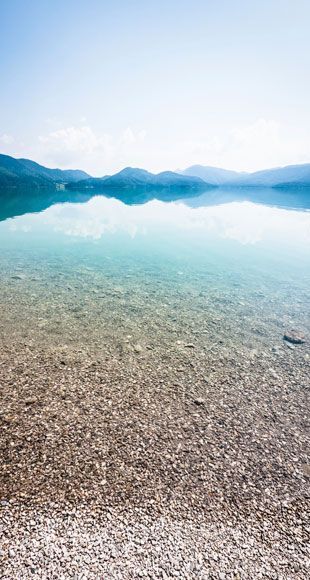 Un lago con montañas al fondo y una playa rocosa en primer plano.
