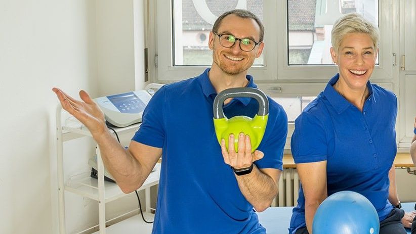 Ein Mann und eine Frau stehen nebeneinander in einem Raum und halten eine Kugelhantel in der Hand.