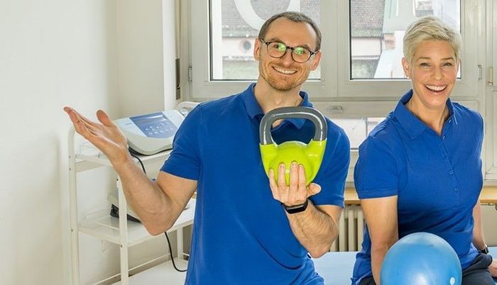 Ein Mann und eine Frau posieren für ein Foto und halten dabei eine Kettlebell und einen Pilatesball.