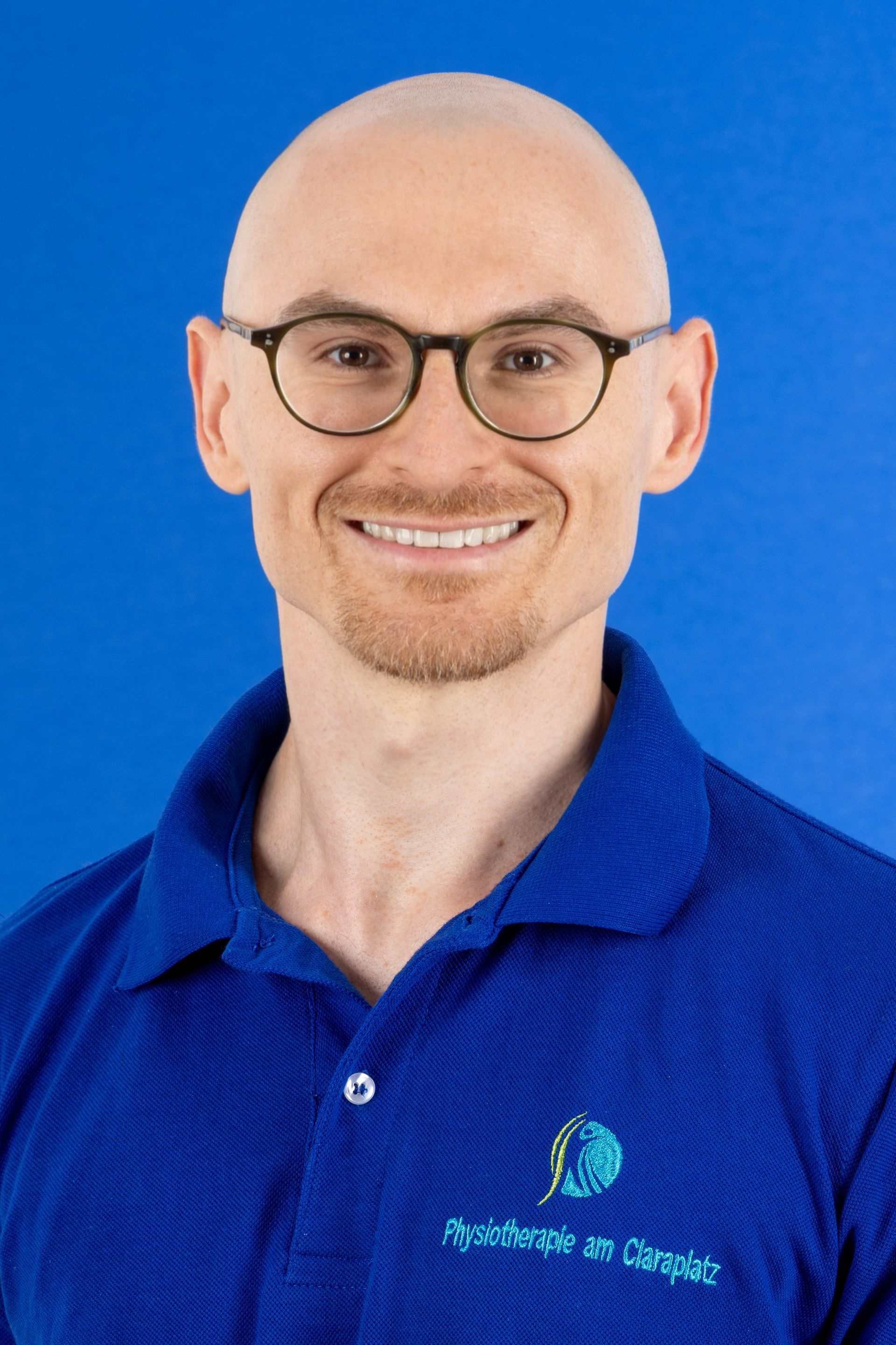 Ein Mann mit Brille und blauem Poloshirt lächelt.