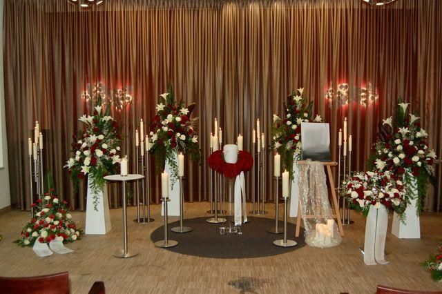 Trauerfeier: Blumenschmuck, Kerzen und ein Erinnerungsfoto auf einer Bühne mit braunen Vorhängen.