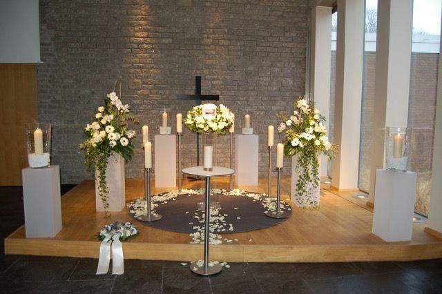 Traueraltar mit weißen Blumen, Kerzen und einem kleinen Kreuz, auf einer erhöhten Holzplattform.
