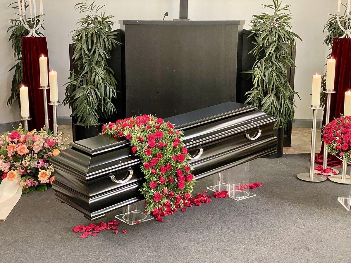 Ein schwarzer Sarg mit roten Rosen bei einer Trauerfeier.