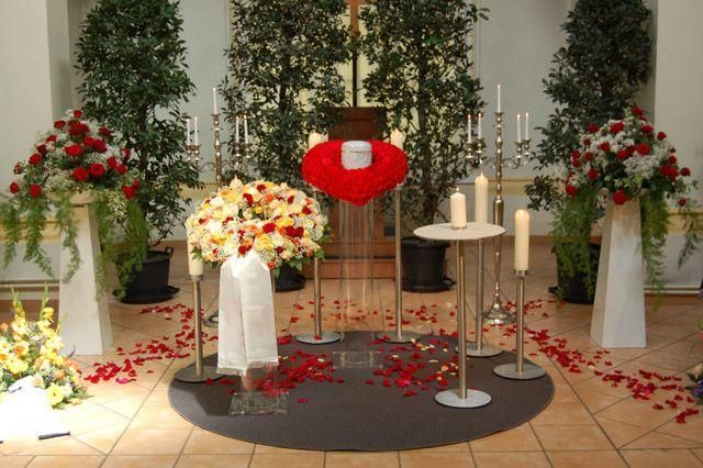 Trauerdekoration mit Blumen, Kerzen und herzförmigem Arrangement um eine weiße Urne.