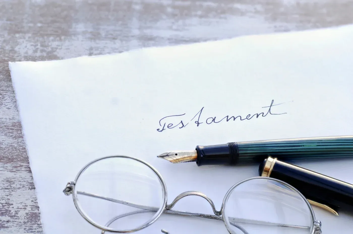 Ein handschriftliches Dokument mit der Aufschrift „Testament“ mit Füllfederhalter und runder Brille.