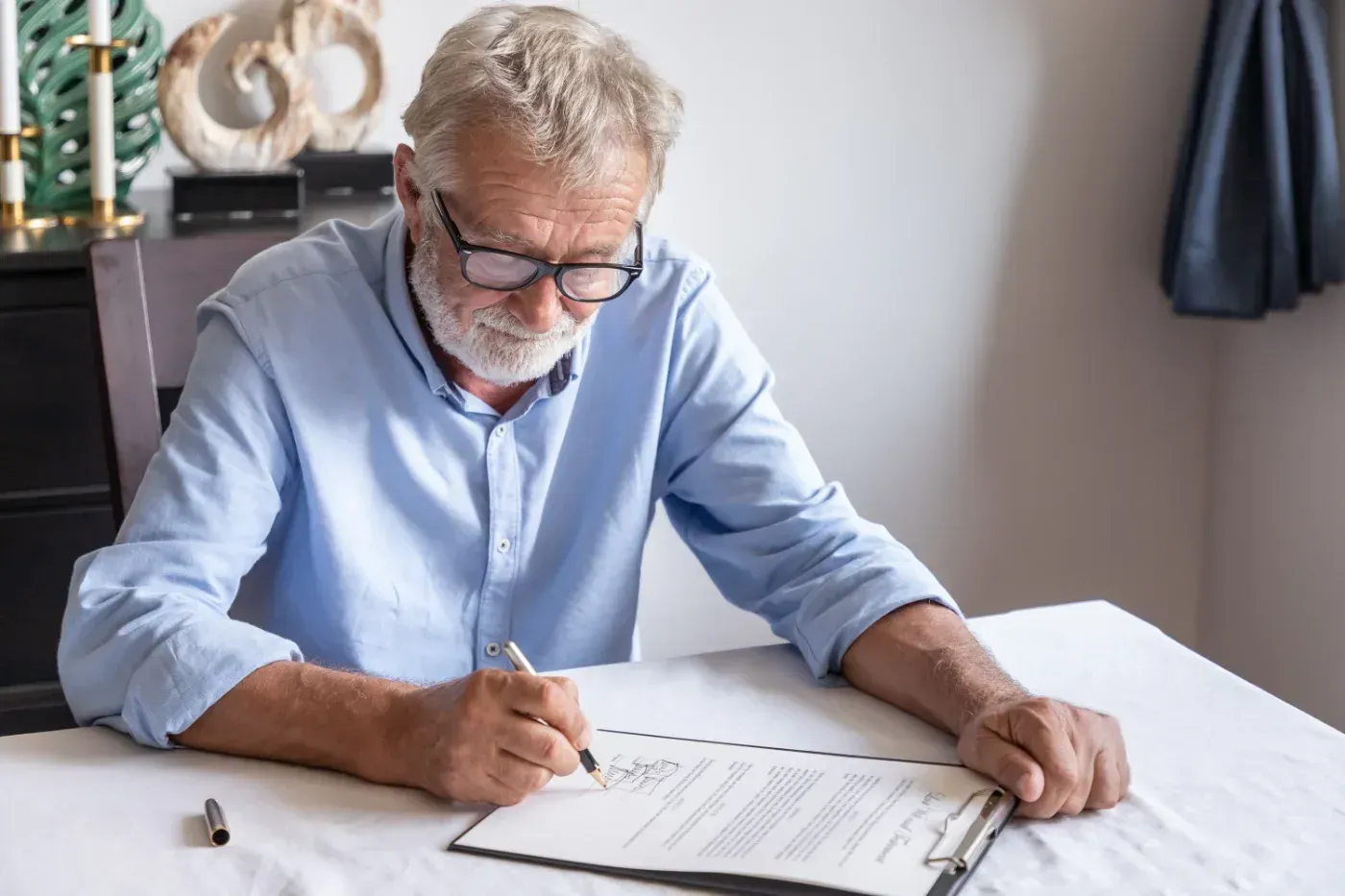 Älterer Mann mit Brille schreibt an einem Tisch auf Papier.