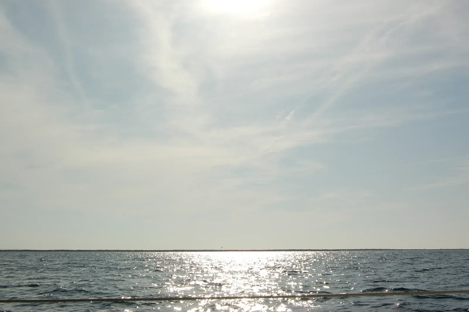 Helles Sonnenlicht spiegelt sich auf einem Gewässer unter einem bewölkten blauen Himmel.