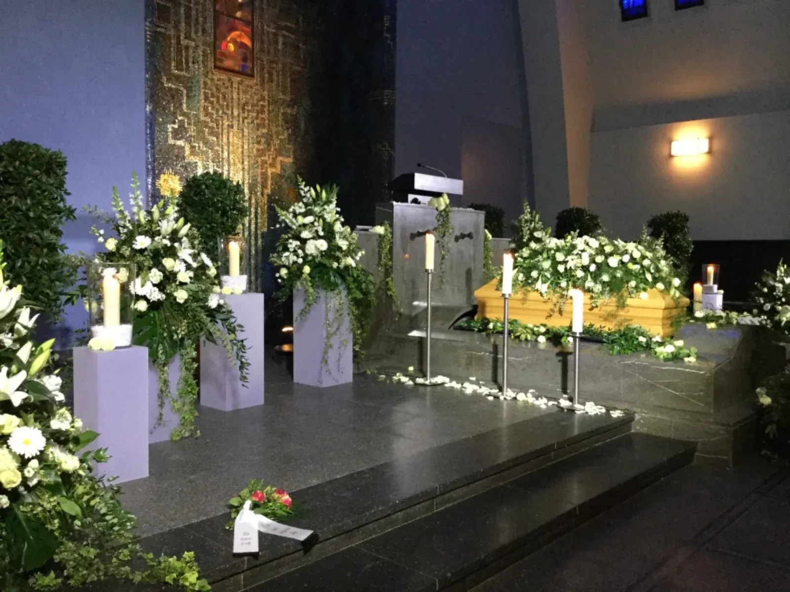 Trauerfeier, Sarg mit weißen Blumen geschmückt, Kircheninnenraum, Blumenarrangements, Kerzen.