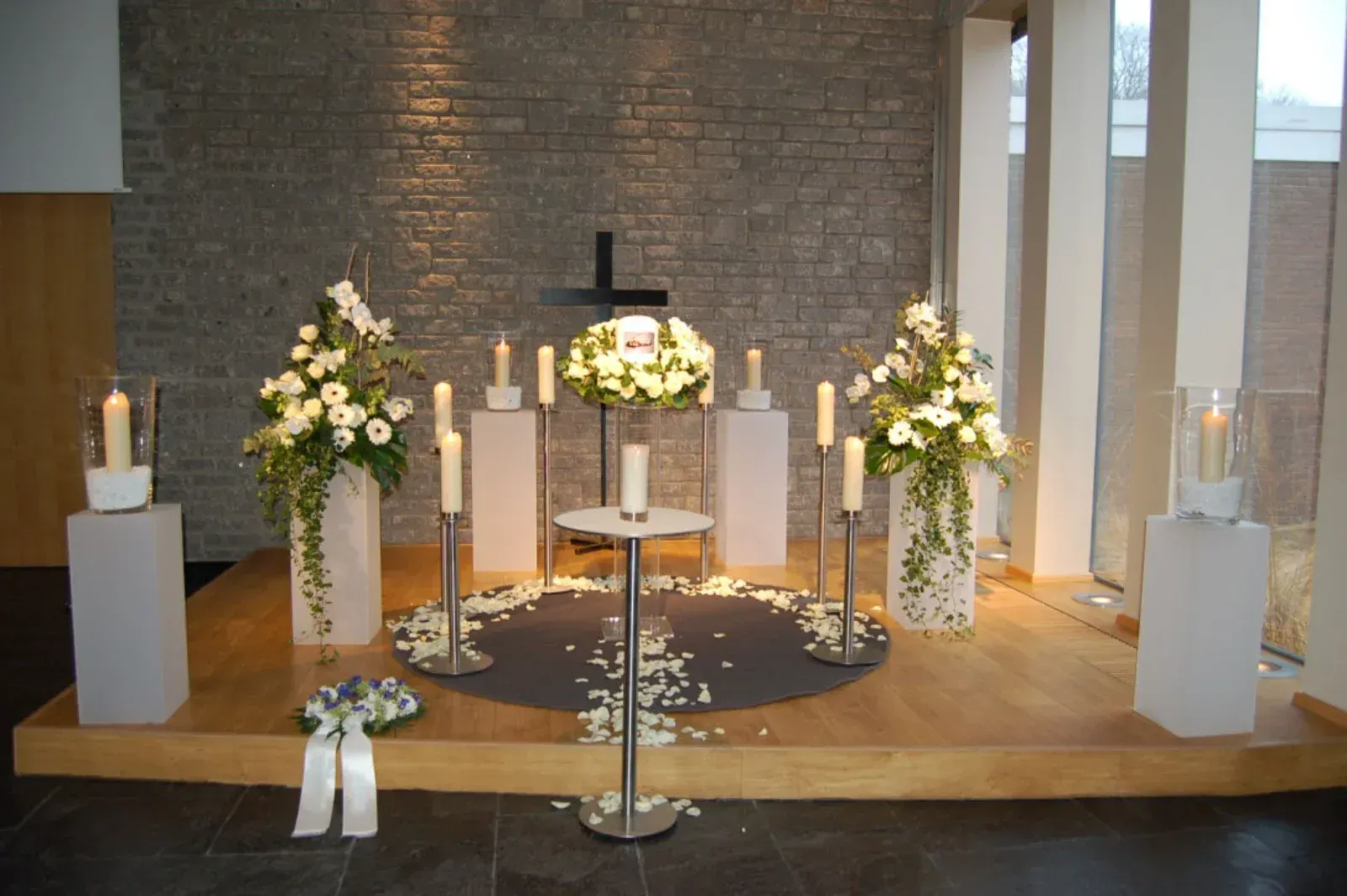 Traueraltar mit weißen Blumen, Kerzen und einem Kreuz auf einer Steinmauer.
