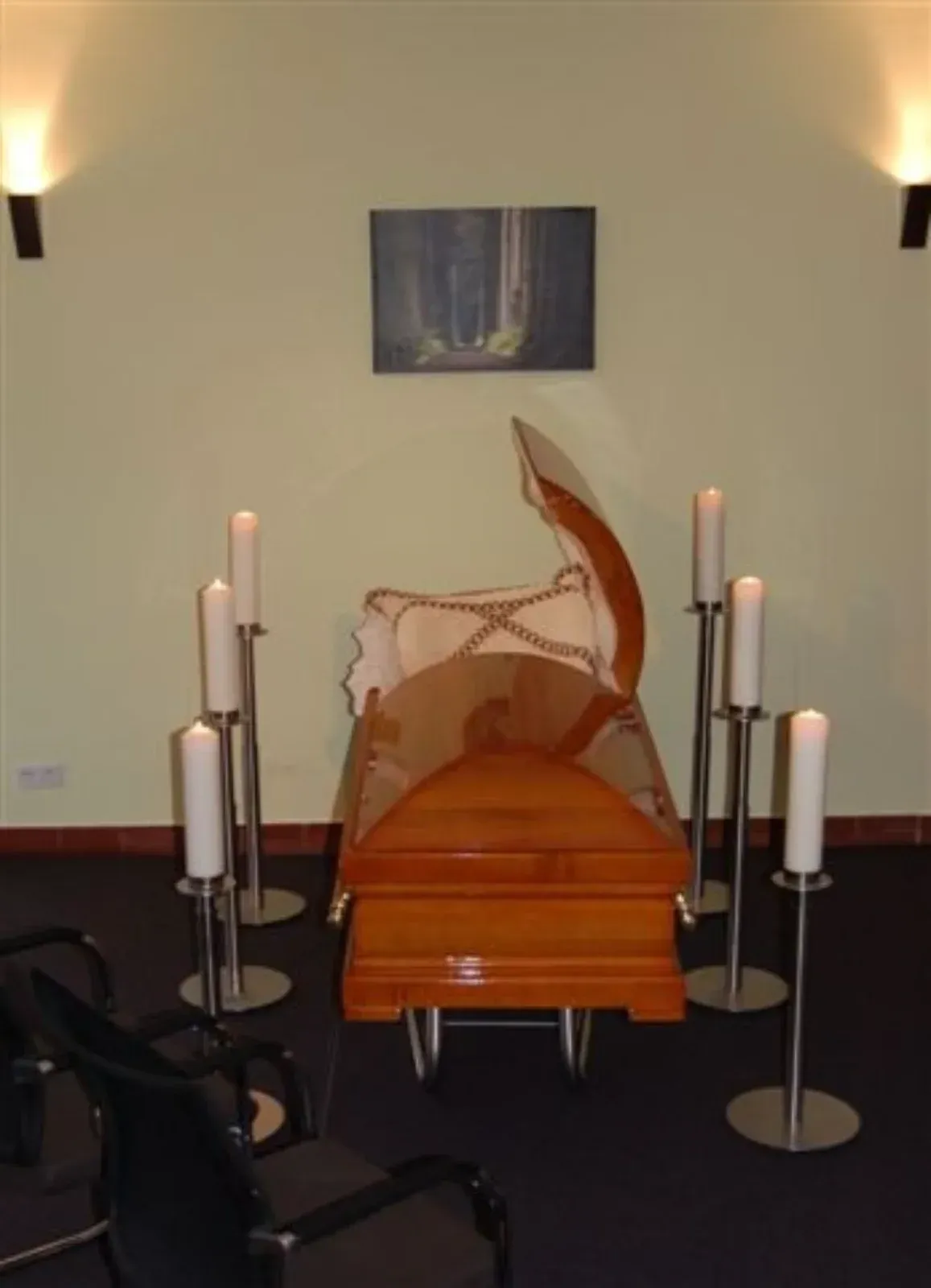 Ein teilweise geöffneter Holzsarg, umgeben von Kerzen in einer schwach beleuchteten Kapelle.