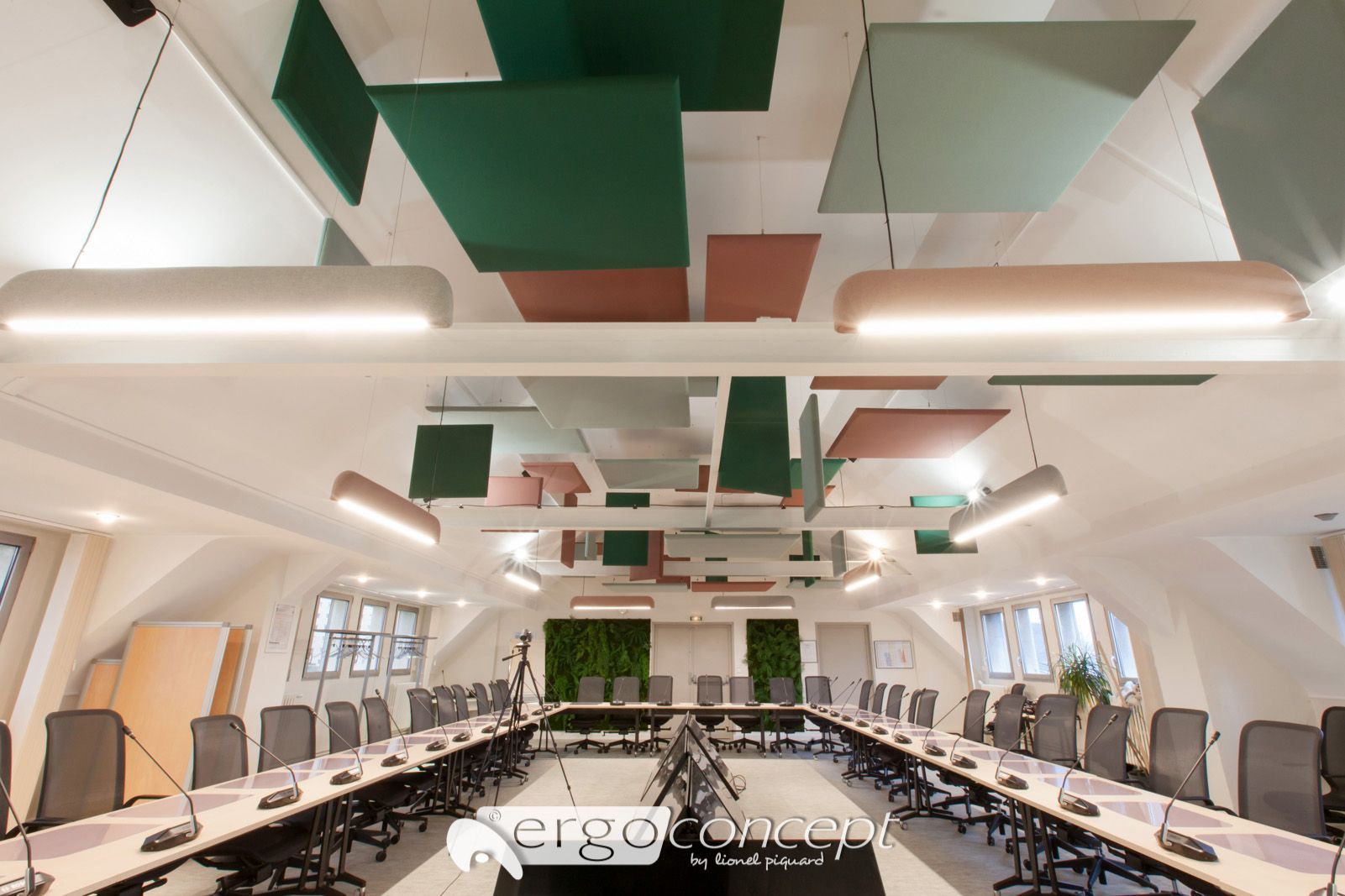 Salle de conférence avec longue table, panneaux de plafond verts et roses et éclairage moderne.