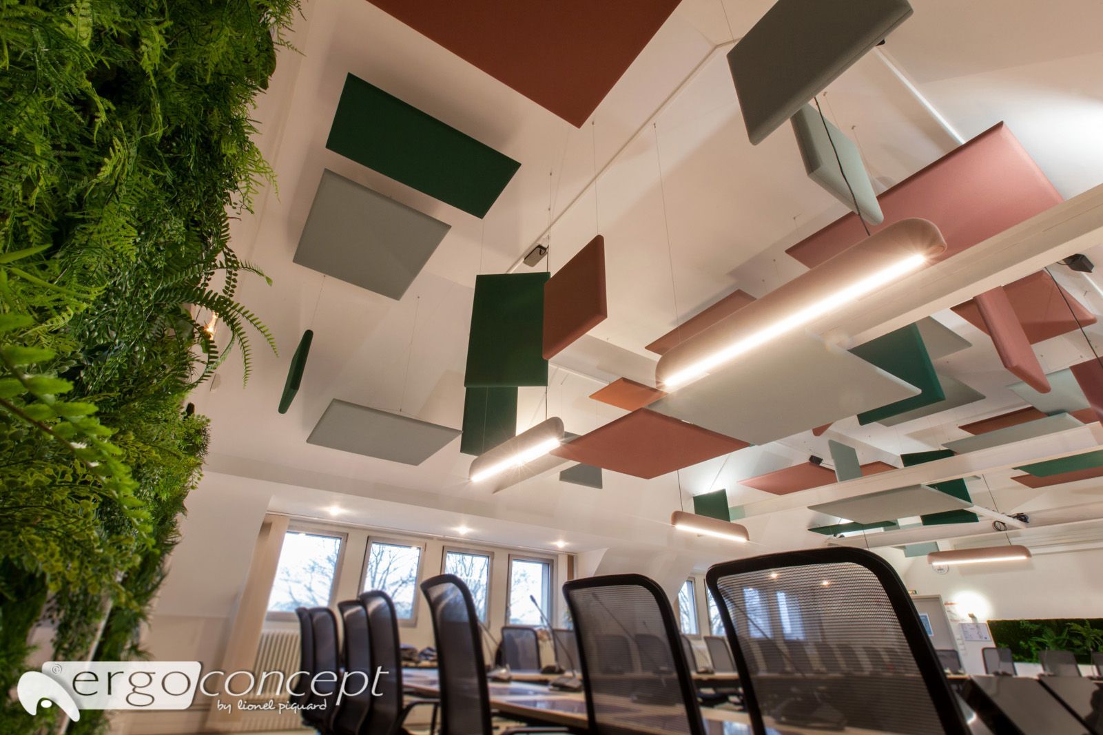 Intérieur de bureau avec un mur végétal, des panneaux de plafond colorés et des chaises.