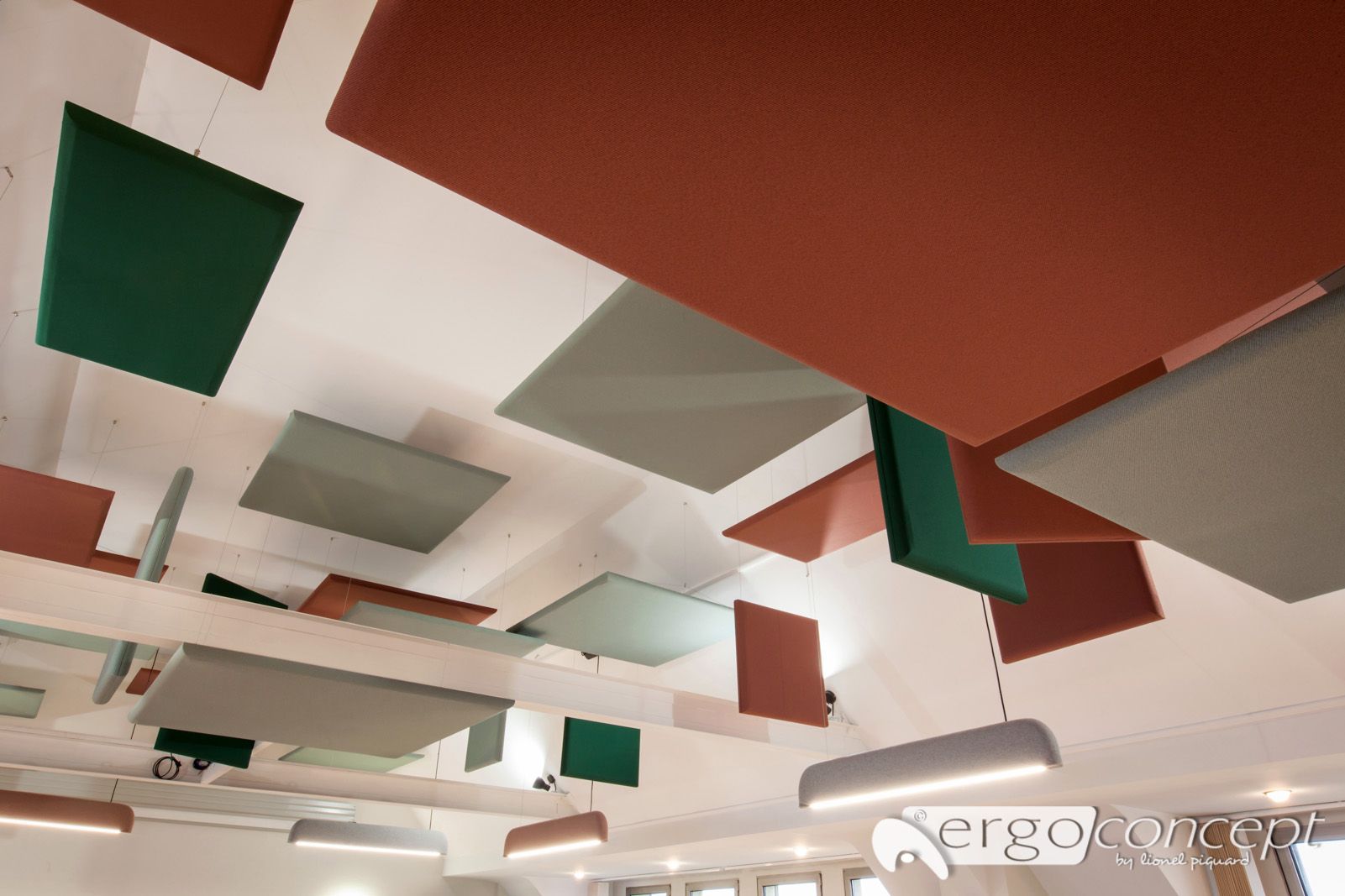 Panneaux acoustiques carrés et colorés suspendus à un plafond blanc, à côté de lumières rectangulaires blanches et élégantes.