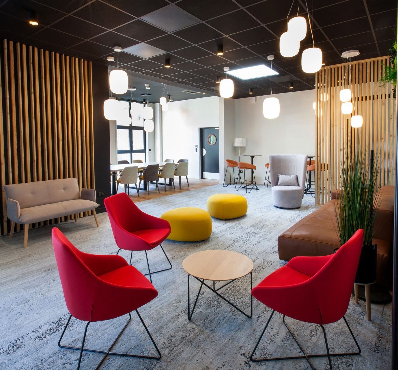 Espace salon moderne avec chaises rouges, touches de bois et divers coins salon.