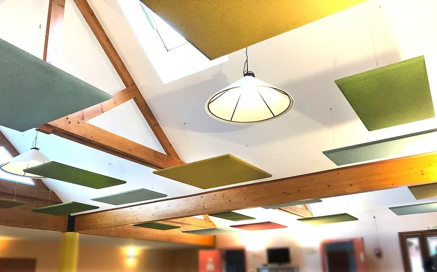 Dans une pièce très lumineuse, salle de restaurant scolaire, plafond haut avec panneaux acoustiques.